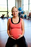 Pregnant woman sitting on fitness ball holding belly.