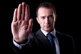 Businessman with his hand raised in signal to stop, isolated on black background, Studio shot