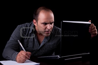 surprised businessman looking to computer and taking notes, isolated on black background. Studio shot.