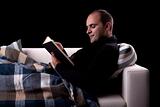 man lying on the sofa reading a book, isolated on black, studio shot.