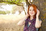 Young  smiling fashion with headphones near tree.