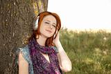 Young  smiling fashion with headphones near tree.