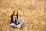 Beautiful red-haired girl sitting at yellow autumn grass.