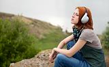 Young fashion girl with headphones at rock near lake.