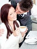 Handsome businessman kissing his girlfriend who is holding a cup