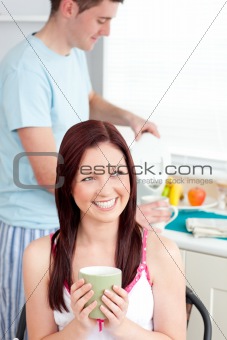 Joyful woman drinking coffee and smiling in the kitchen