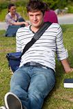 Handsome male student lying on the grass with his schoolbag