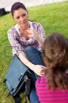 Two female friends talking together sitting on the grass