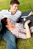 Couple of cheerful students using a laptop lying on the grass