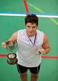 Sporty man holding a cup and a medal standing on a games field