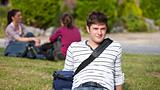 Positive male student lying on the grass with his schoolbag