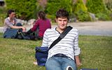 Good-looking male student lying on the grass with his schoolbag