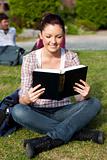 Young female student reading a book sitting on grass