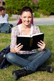 Serious female student reading a book sitting on grass