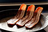 three stripes of bacon in a pan