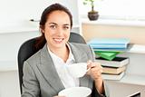 Happy businesswoman holding a cup of coffee sitting in her offic