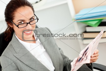 smiling businesswoman holding her glasses and reading a newspaper