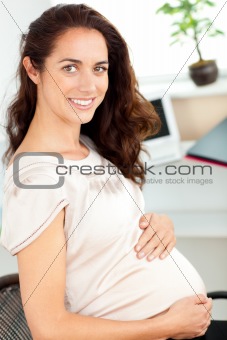 Pregnant businesswoman smiling at the camera sitting at her desk
