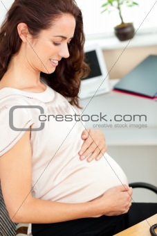 Pregnant businesswoman touching her belly sitting at her desk