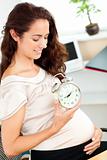 Pregnant businesswoman holding an alarm clock and looking at her