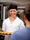 Smiling female baker holding baguettes ready to serve her custom