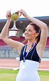 Joyful female athlete holding a trophee and a medal