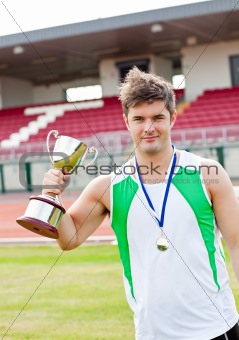 Delighted male athlete holding a cup and a medal standing