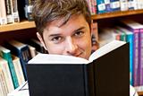 Portrait of a good-looking male student reading a book sitting o
