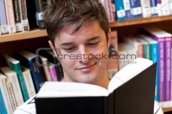 Portrait of a smiling male student reading a book sitting on the