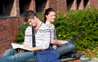 Lovely couple of students using a laptop and reading a book