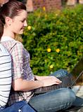 Charming female student using a laptop and sitting behind her bo