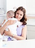 Positive young mother holding her baby in the kitchen