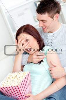 Young couple lying on the sofa with popcorn and remote