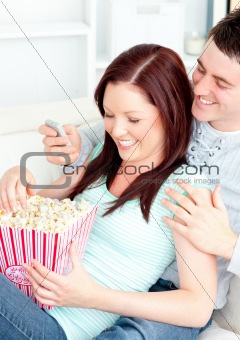 Bright young couple lying on the sofa with popcorn and remote