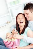 Laughing young couple lying on the sofa with popcorn and remote