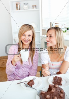 Happy female friends eating a chocolate cake and drinking in the