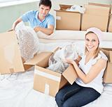 Merry young couple unpacking boxes with glasses