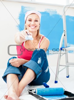 Joyful young woman holding a paint brush smiling at the camera