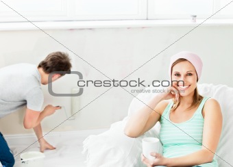 Smiling caucasian woman relaxing on a sofa while boyfriend paint