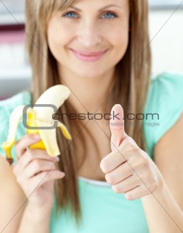 Smiling woman with thumb up holding a banana in the kitchen