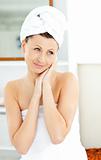 Charming young woman with a towel putting cream on her face in t