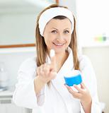 Pretty young woman using cream wearing a bath robe in the bathro