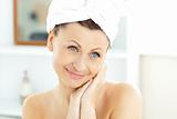 Radiant young woman with a towel putting cream on her face in th