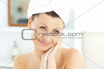 Radiant young woman with a towel putting cream on her face in th