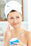 Positive young woman with a towel putting cream on her face in t