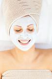 Merry young woman with white cream on her face relaxing on a mas