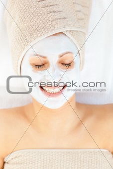 Merry young woman with white cream on her face relaxing on a mas