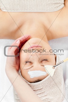 Relaxed young woman receiving white cream on her face