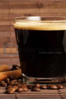 espresso in a short glass with coffee beans and cinnamon from side