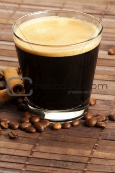 espresso in a short glass with coffee beans and cinnamon from diagonal top